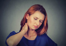 A woman holding her neck with painful expression.