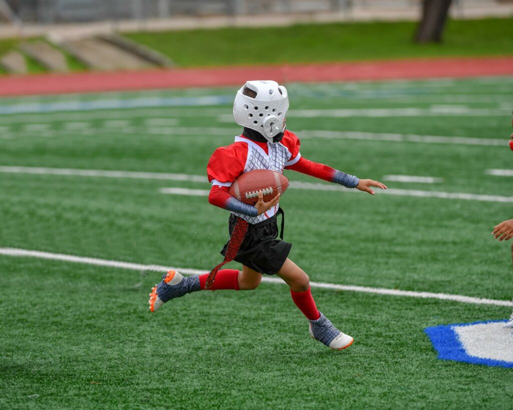 Young athletic boy wearing a helmet catching, running and throwing the ball in a football game